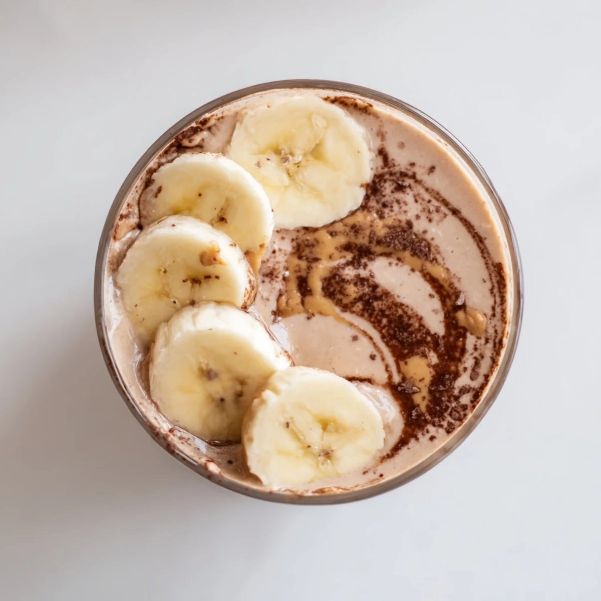 Vibrant morning light highlights a tall glass of Chocolate Peanut Butter Smoothie beside a banana and peanut butter jar.