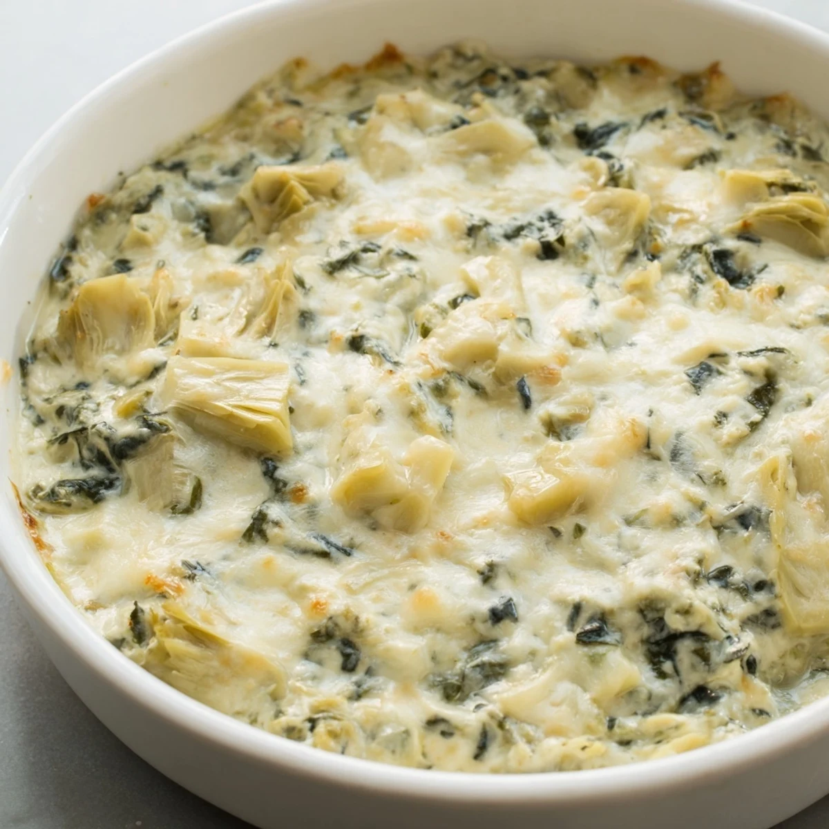 Golden baked spinach and artichoke dip bubbling in a dish, served with crisp tortilla chips for a party appetizer.