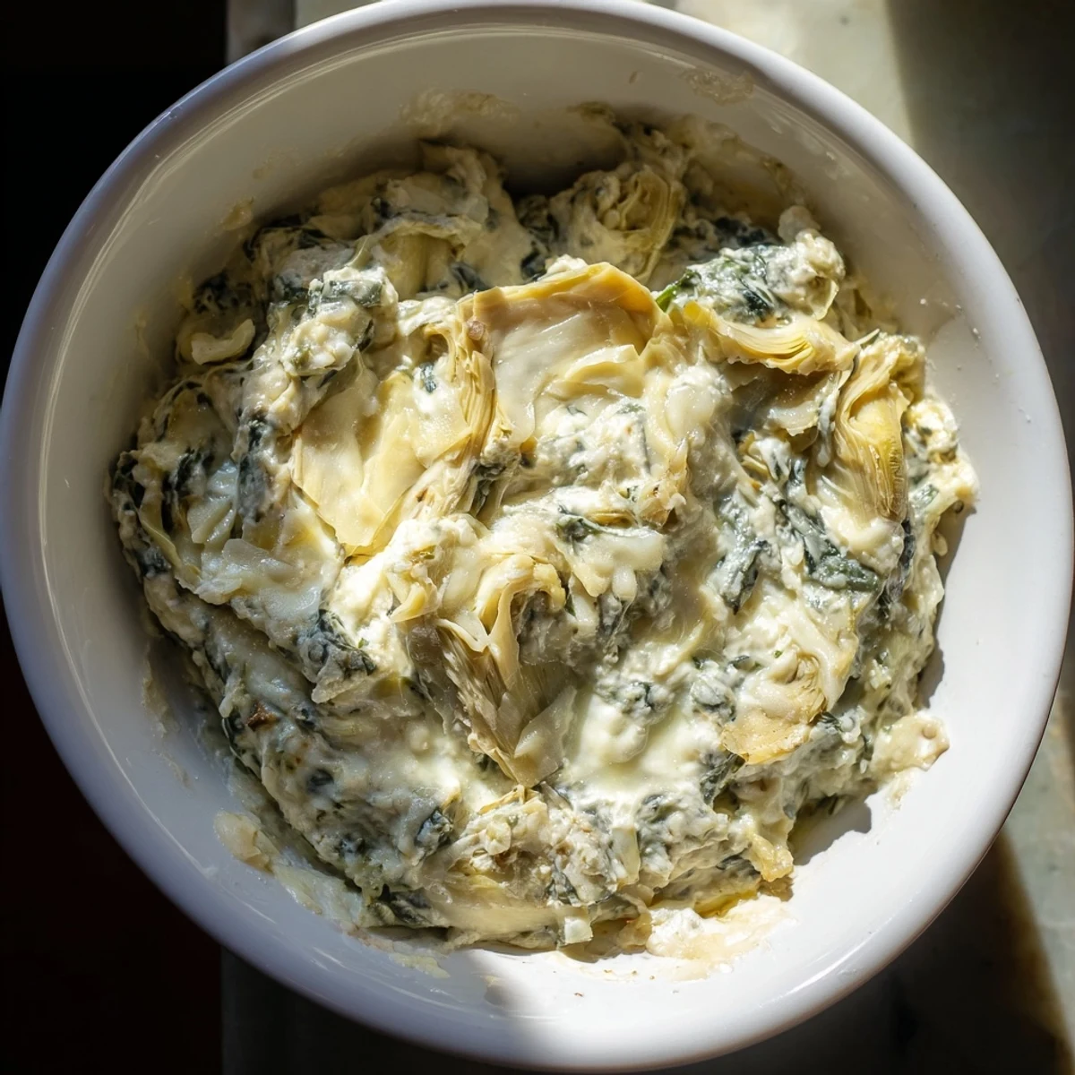 Creamy Spinach Dip with Artichokes and Cheese served warm with crunchy sliced baguette and fresh vegetables on a rustic wooden table.