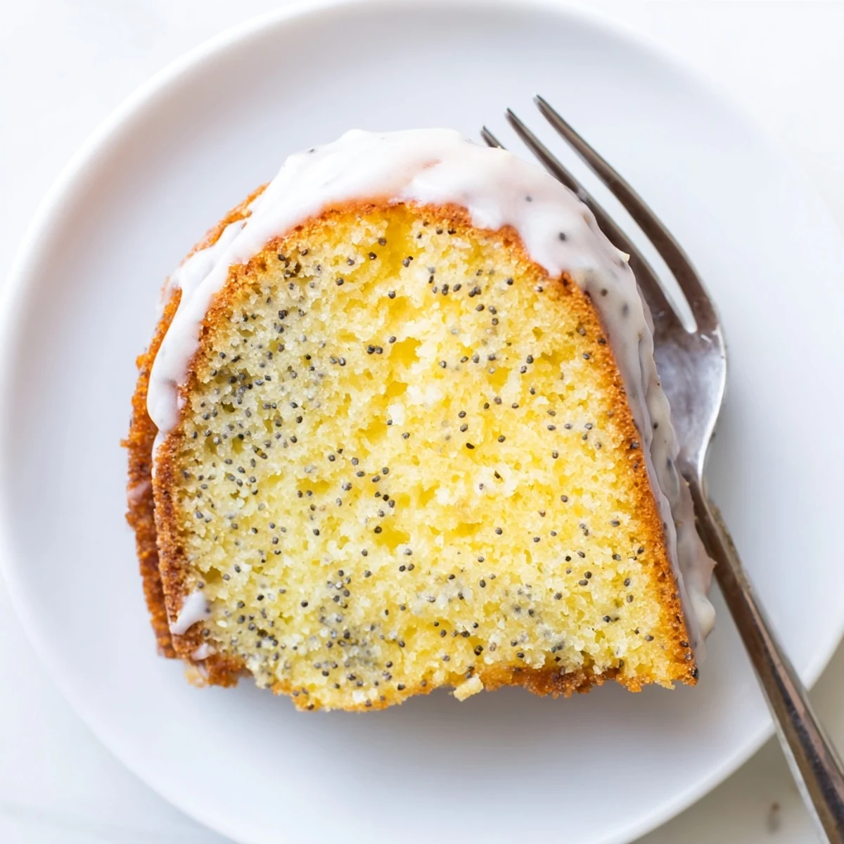 Freshly baked Lemon Poppy Seed Bundt Cake with Glaze dusted with poppy seeds on a marble countertop.