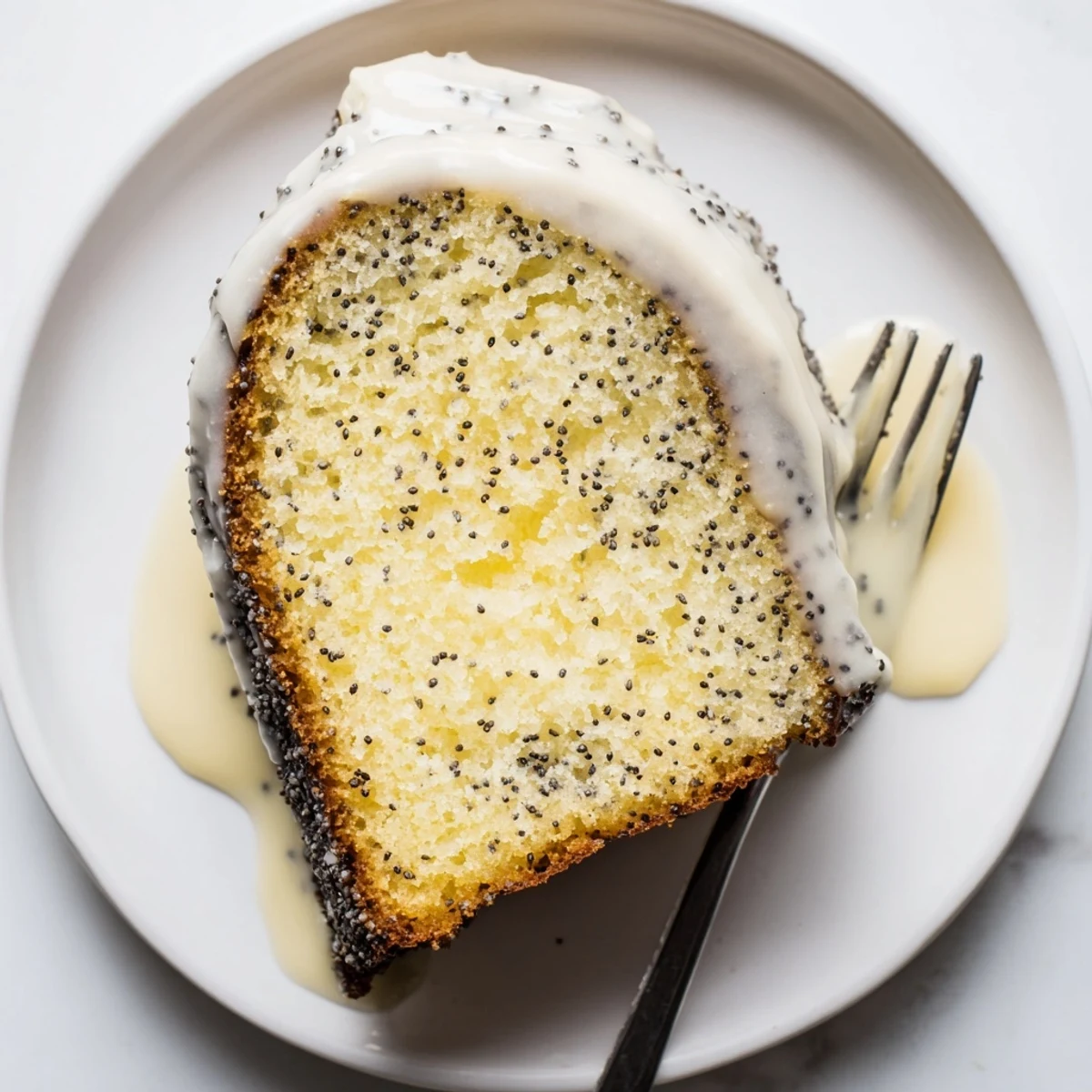 Overhead view of Lemon Poppy Seed Bundt Cake with Glaze being sliced to reveal tender interior texture.