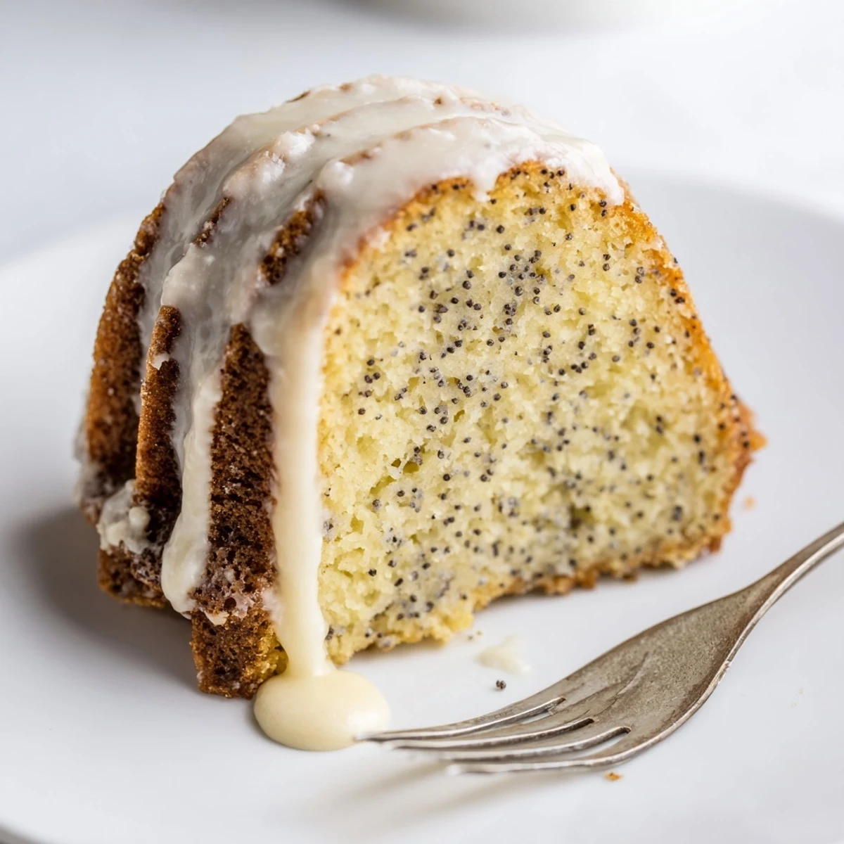 A close-up of a slice of Lemon Poppy Seed Bundt Cake reveals moist crumb with poppy seeds and lemon glaze drip.