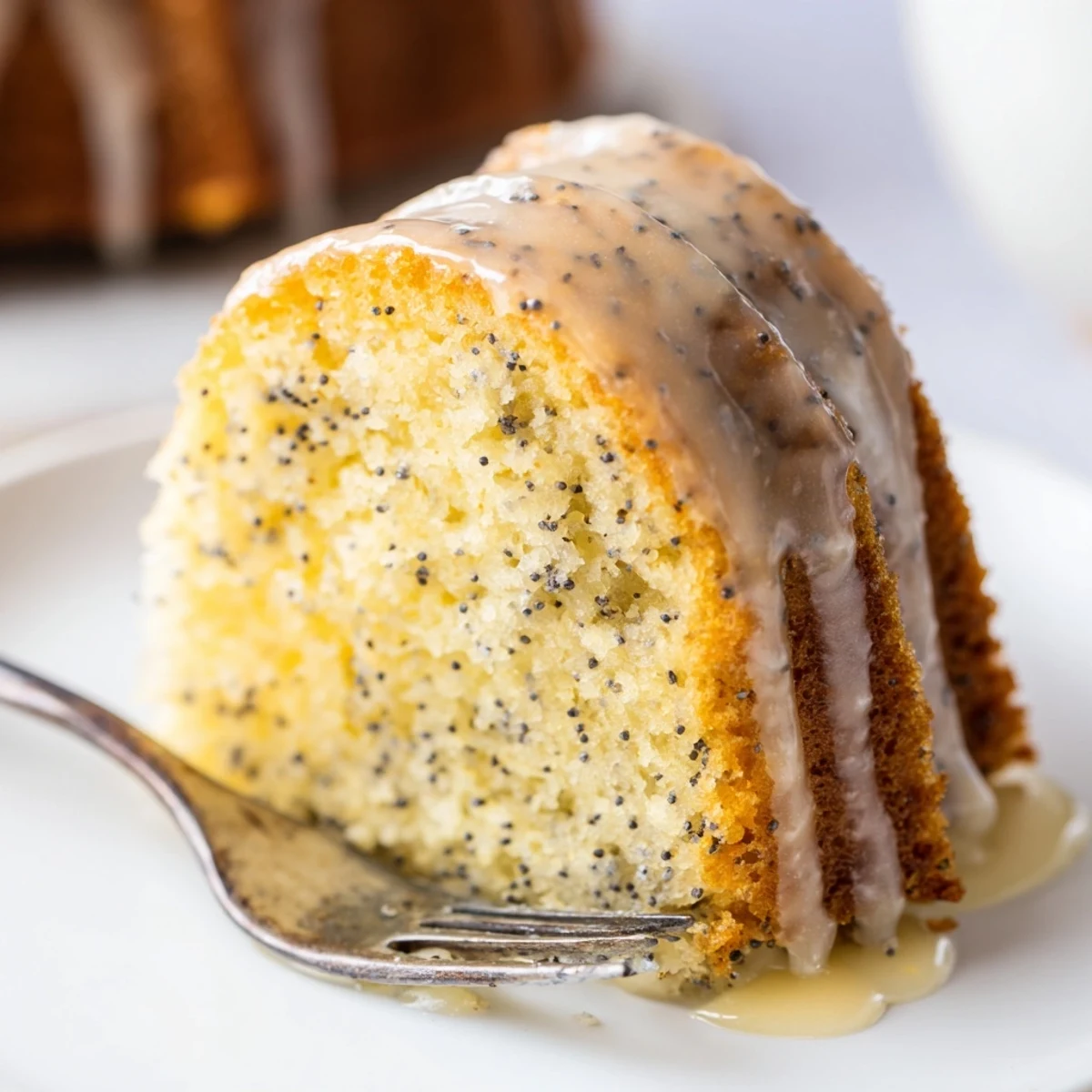 Perfectly formed Lemon Poppy Seed Bundt Cake sits on a serving plate with a lemon slice and tea for brunch.
