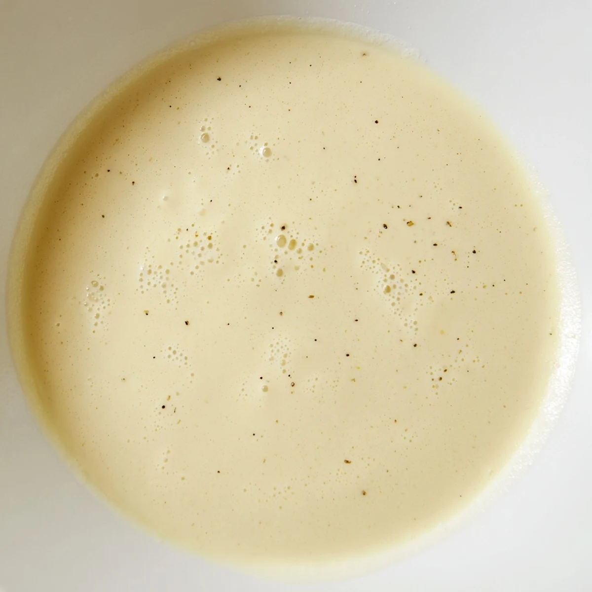 Bright yellow lemon dijon dressing coats a wooden spoon, with fresh herbs and garlic nearby for serving.