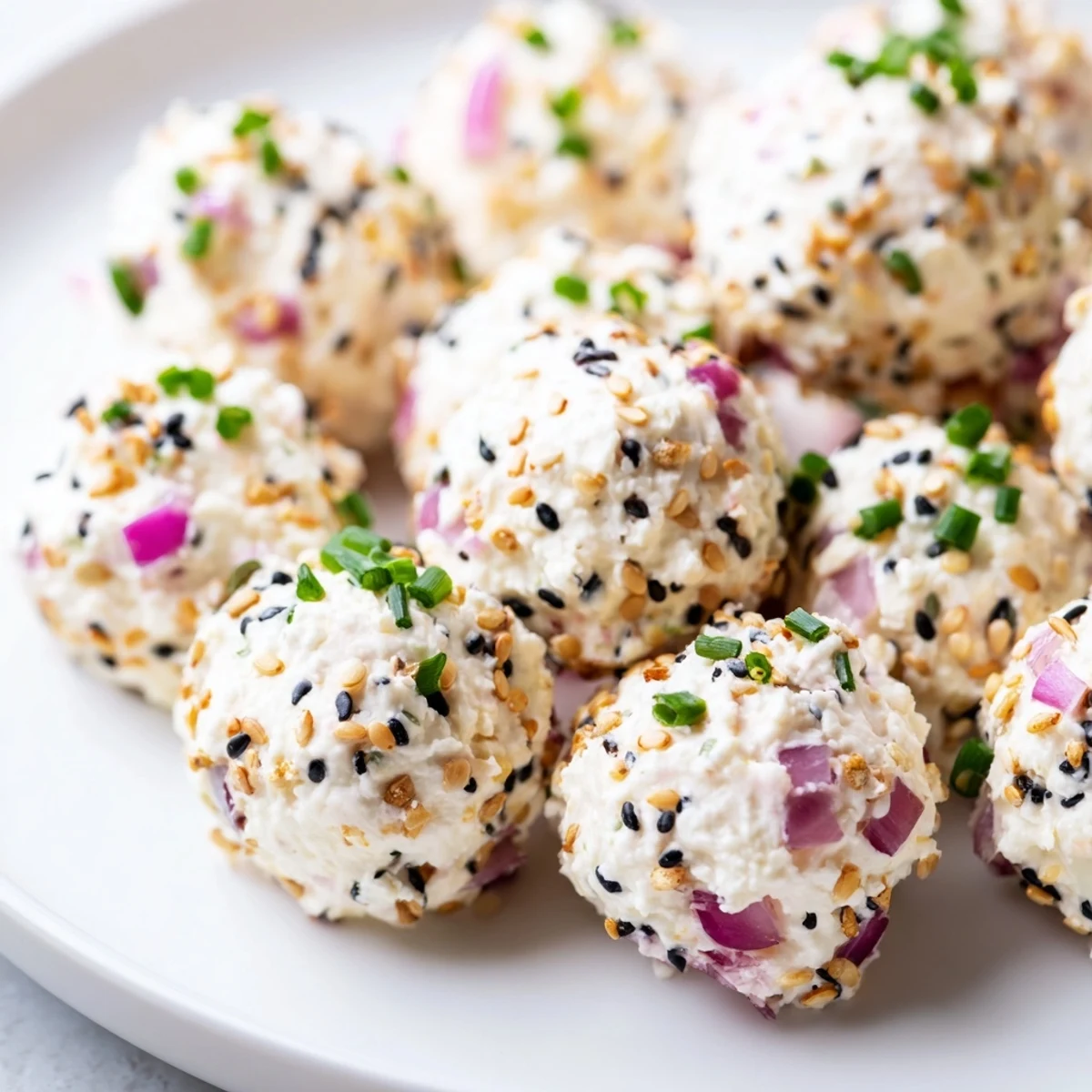 Everything Bagel Cottage Cheese Bites are coated in savory seasoning and arranged on a white plate with fresh chives and cucumber slices.