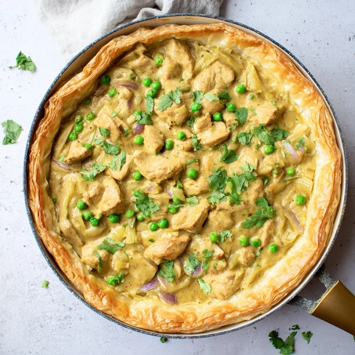 A close-up of golden, flaky One Pan Chicken Korma Pie bubbling from an ovenproof skillet, with steam rising and cilantro garnish.