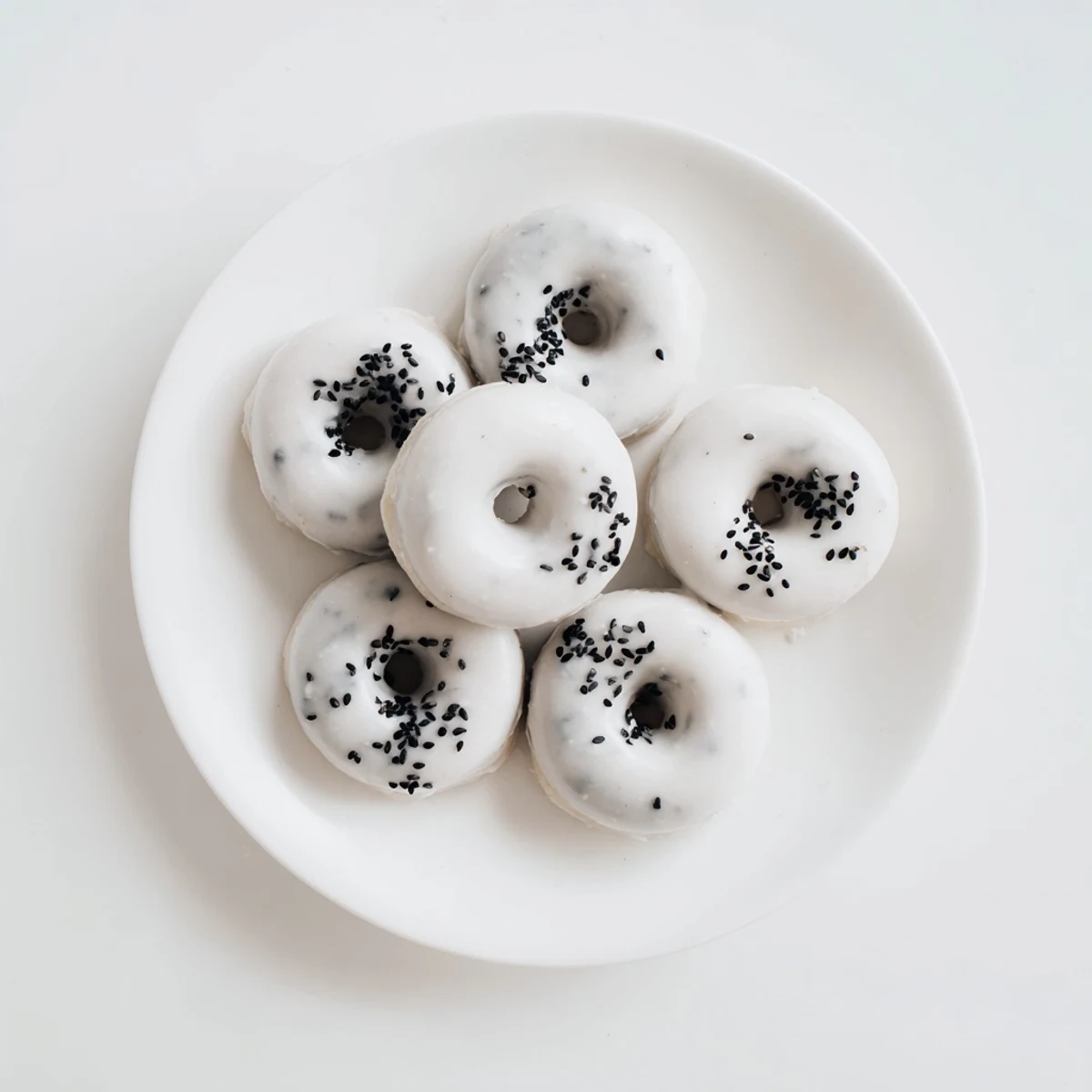 A close-up view of freshly baked Black Sesame Mochi Donuts arranged on a wooden board, each with a glossy black sesame glaze and a sprinkle of extra seeds.