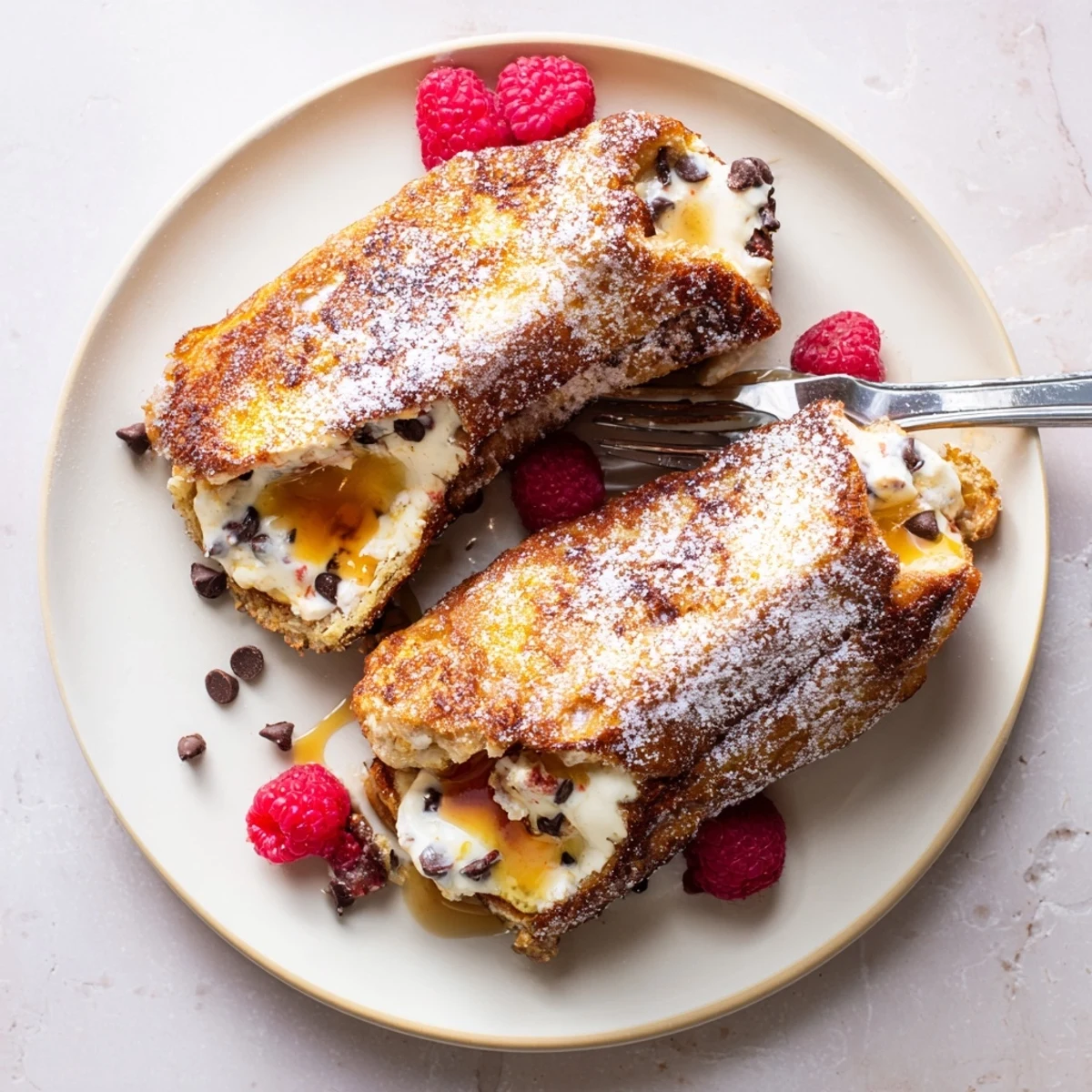 Close-up view of Decadent Cannoli Stuffed French Toast, featuring a crispy exterior and rich filling dusted with powdered sugar and fresh fruit.