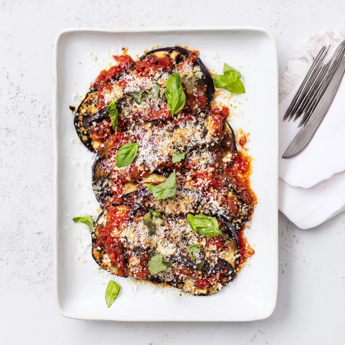 A close-up of Charred Aubergine Parmigiana with charred eggplant slices and fresh basil garnish served in a baking dish.