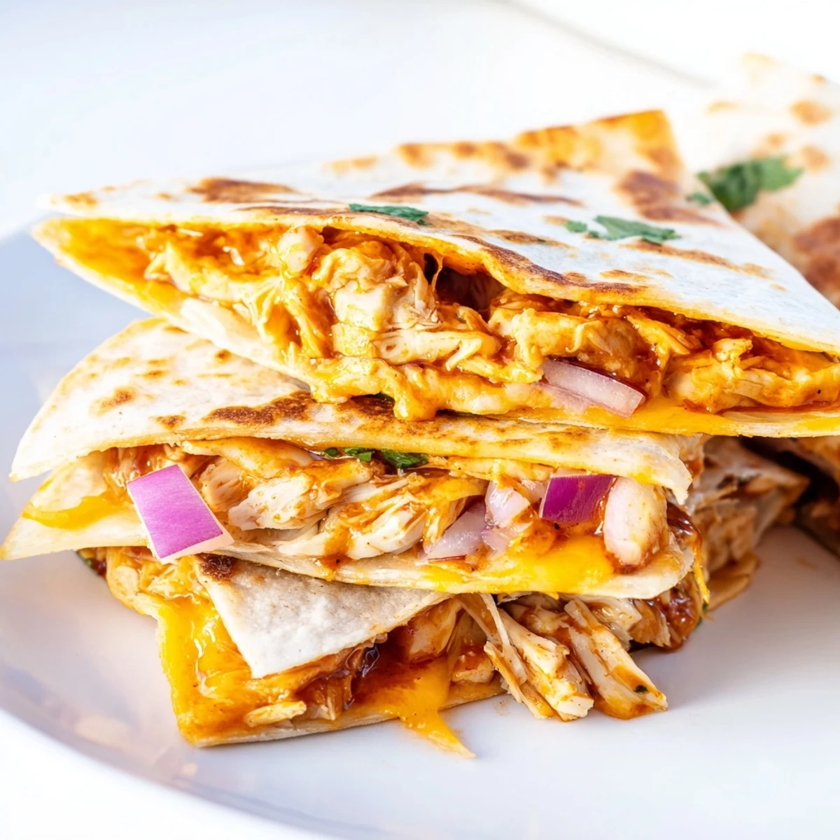 Hot honey BBQ chicken quesadillas on a white plate, featuring melted cheese and diced red onion garnish, perfect for a quick weeknight dinner.