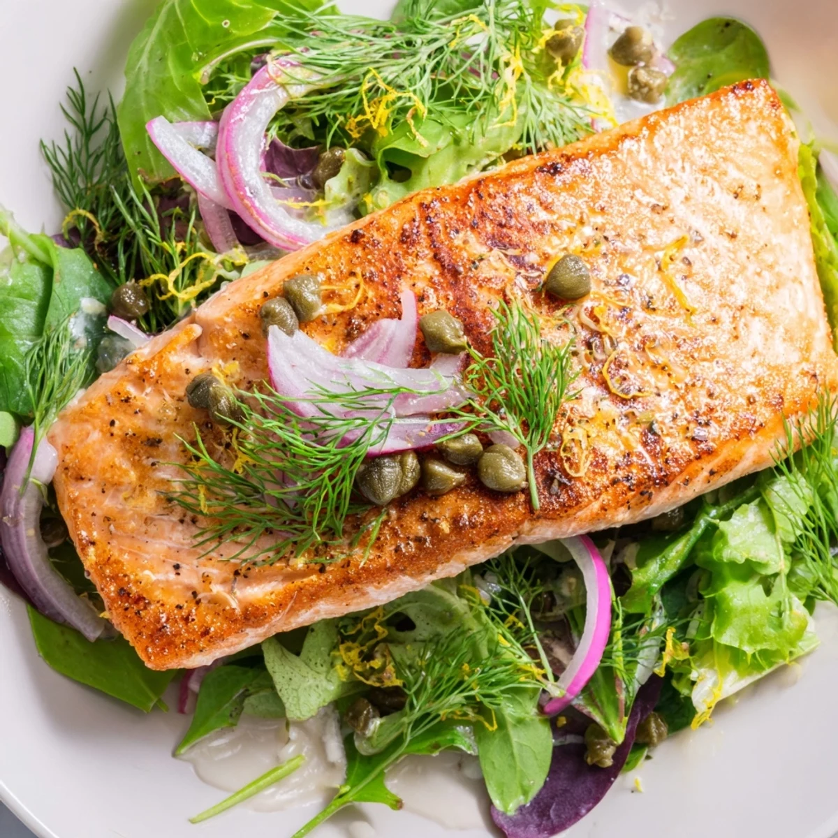 A close-up of perfectly seared Crispy Skin Tasmanian Atlantic Salmon reveals moist flesh and crispy texture, served with capers and lemon zest.