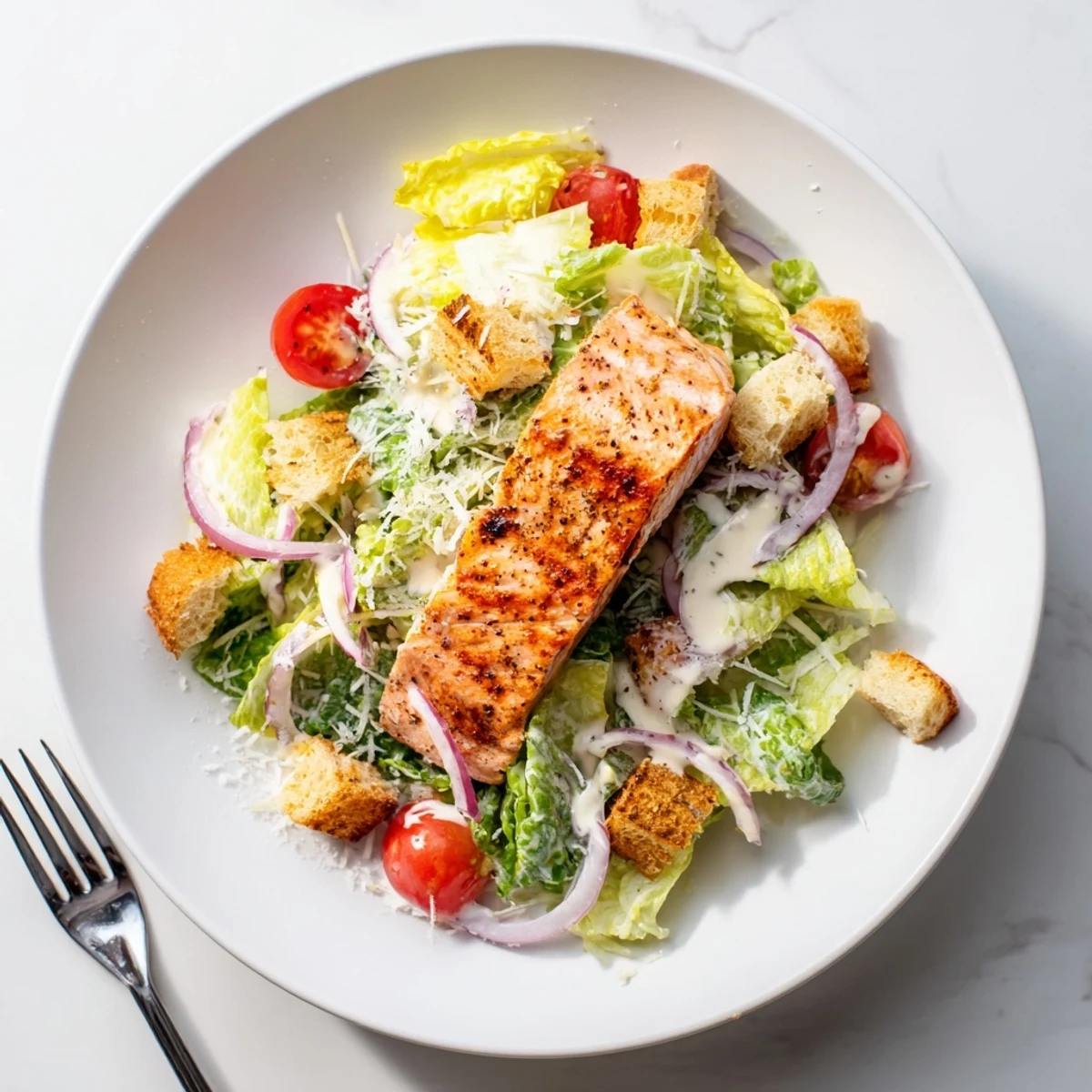 Grilled salmon Caesar salad with crisp romaine, croutons, and creamy homemade dressing served on white plate.