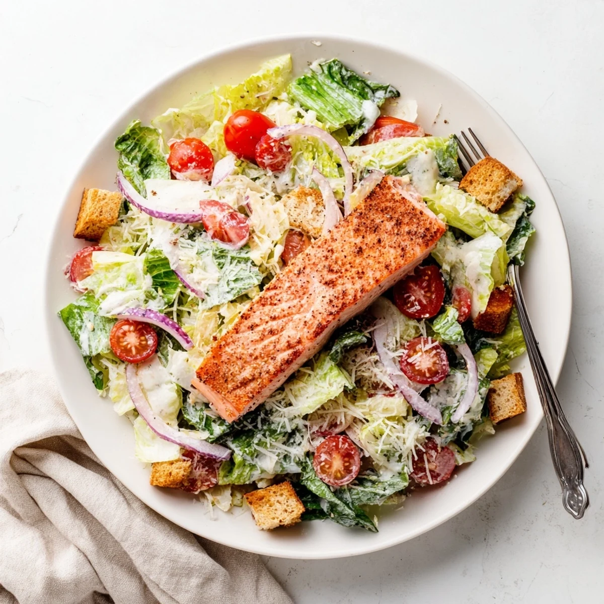Flaky salmon fillet resting atop vibrant Caesar salad with cherry tomatoes, red onion, and Parmesan sprinkles.