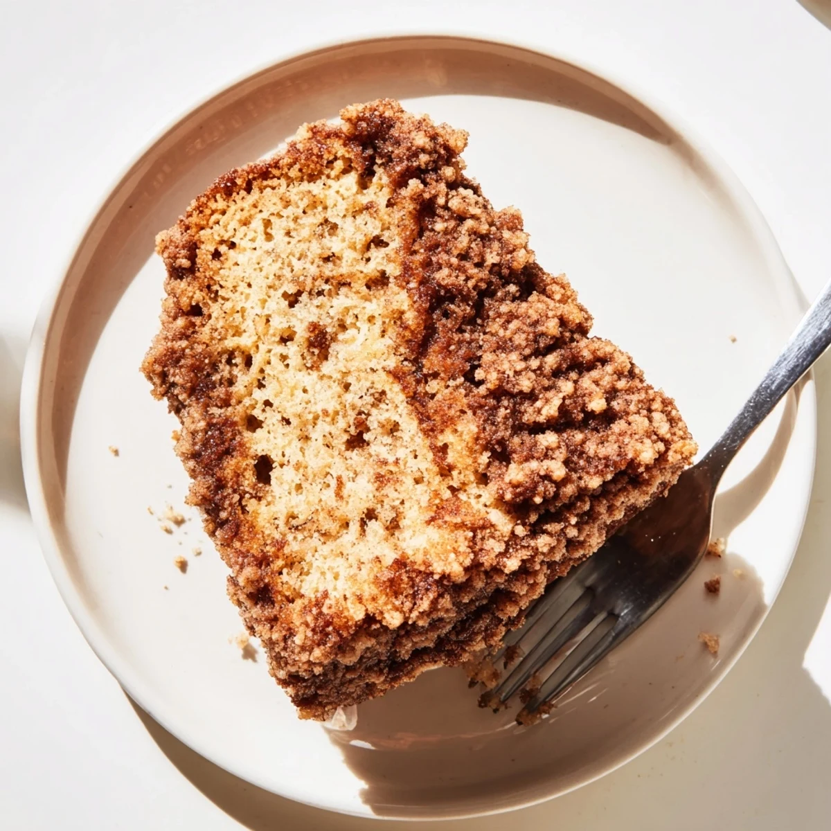 Warm slice of cinnamon crumb banana bread served on white plate with melting butter