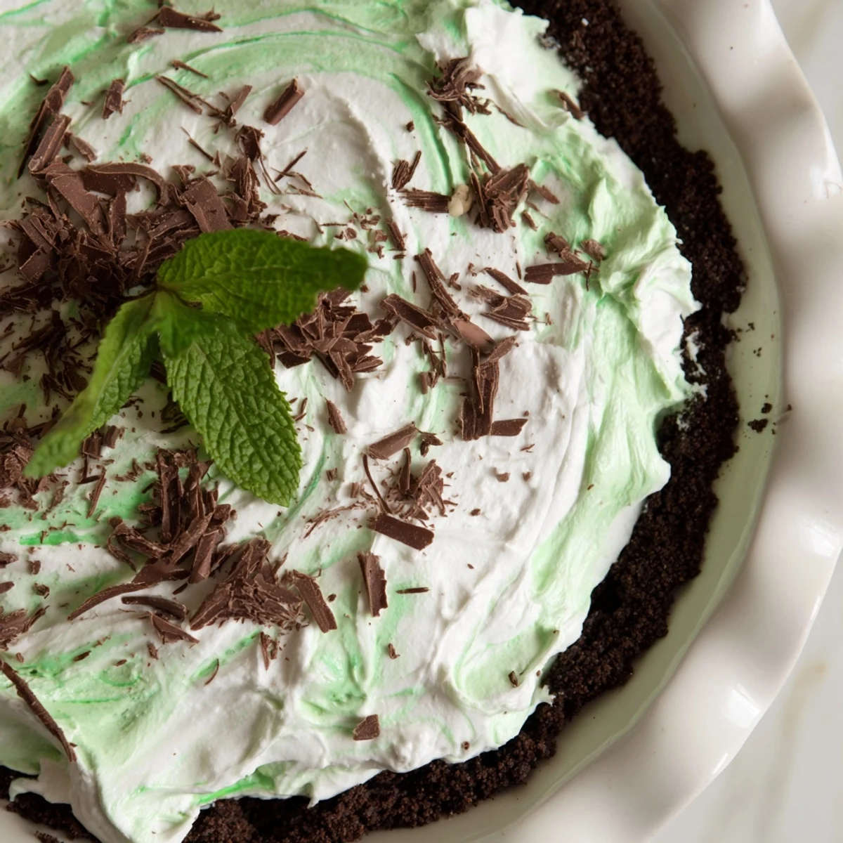 Freshly cut Shamrock Swirl Pie piece topped with whipped cream swirls and chocolate shavings on white plate