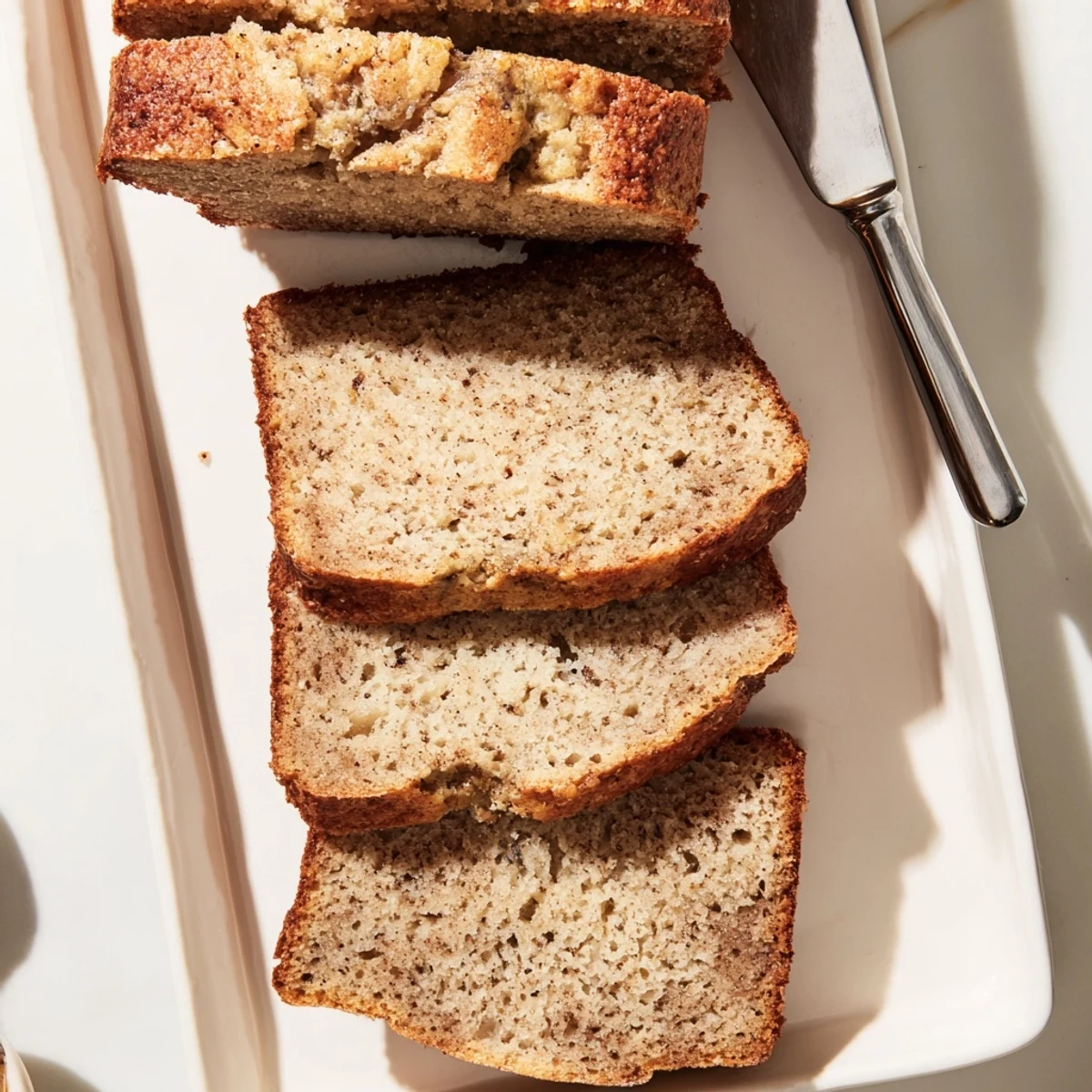 Golden brown moist banana bread loaf sliced on a wooden cutting board with soft texture visible