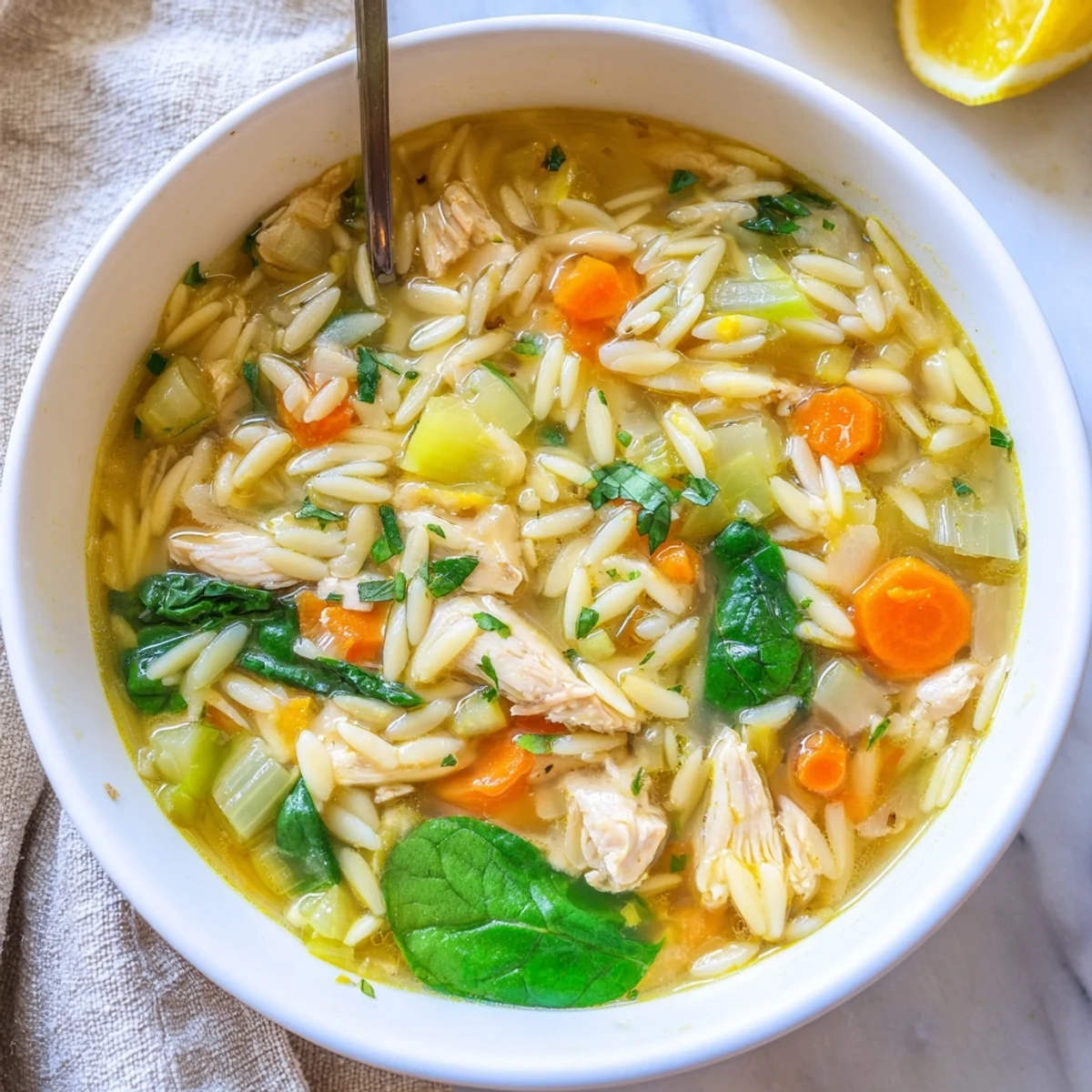 Creamy spring lemon chicken orzo soup in white bowl with fresh parsley garnish