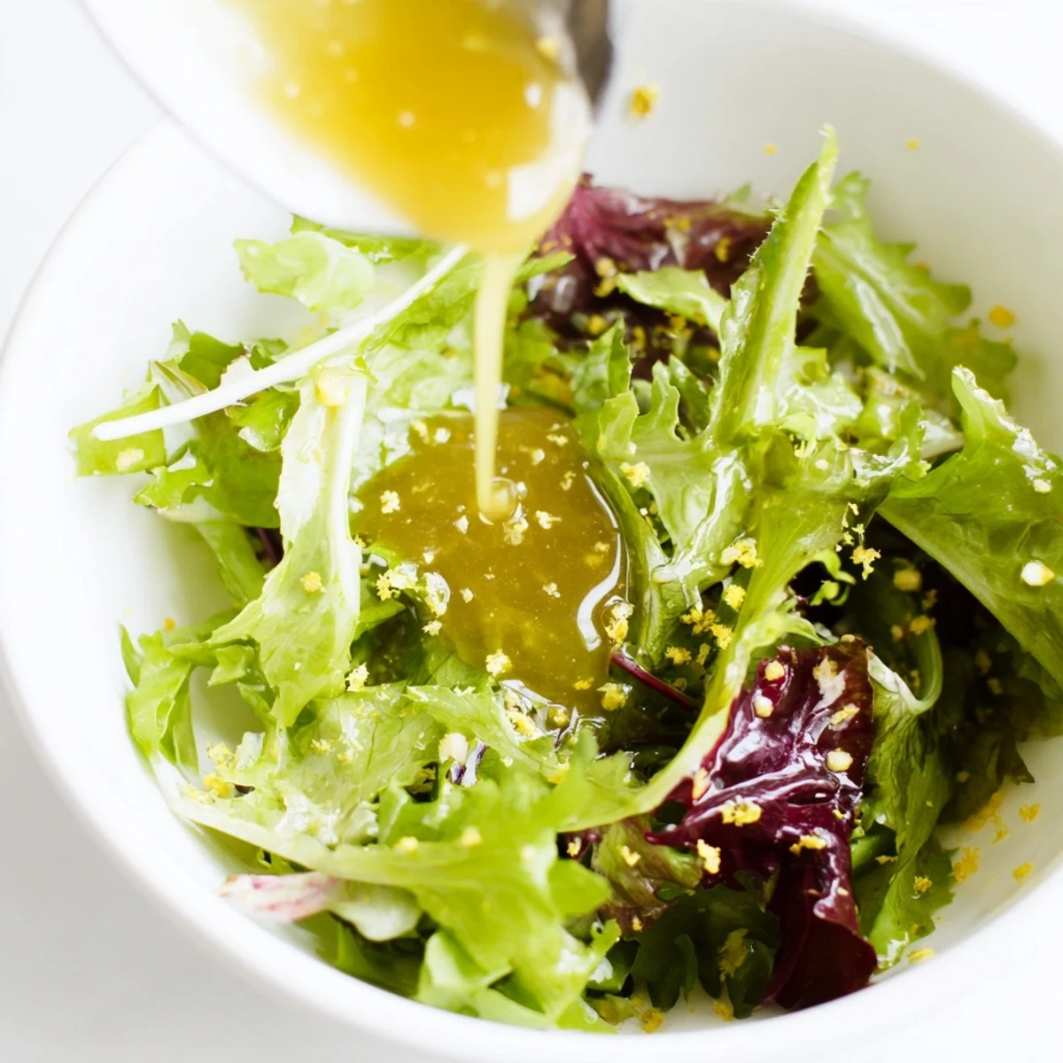 Creamy honey lemon vinaigrette in glass jar with whisk and fresh lemon slices on wooden board