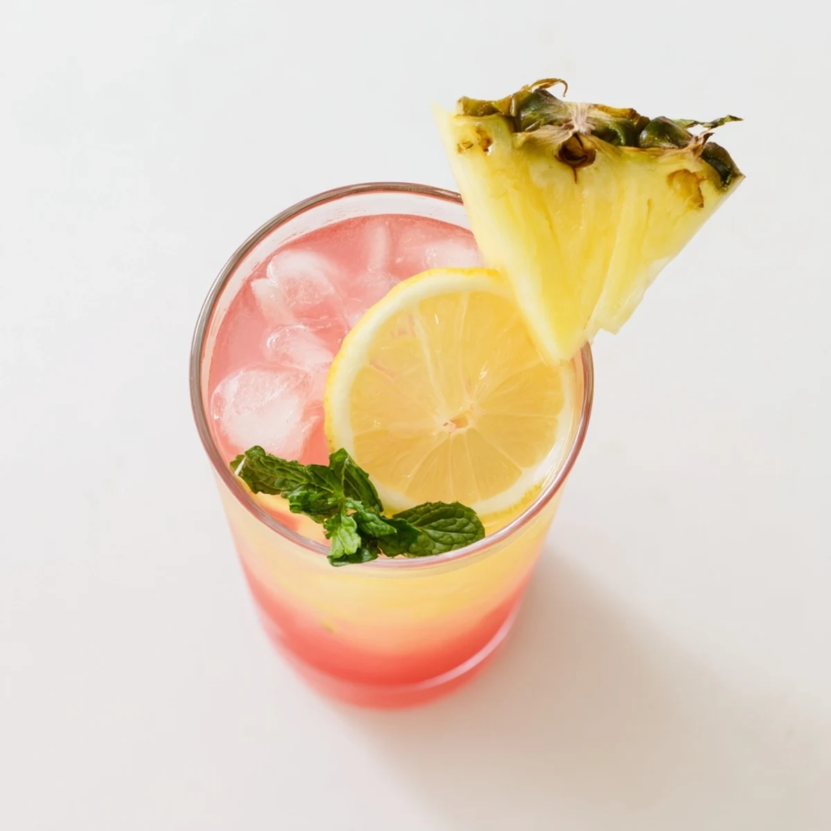 Refreshing pineapple pink lemonade served over ice with pineapple wedge and lemon wheel garnish on a wooden table