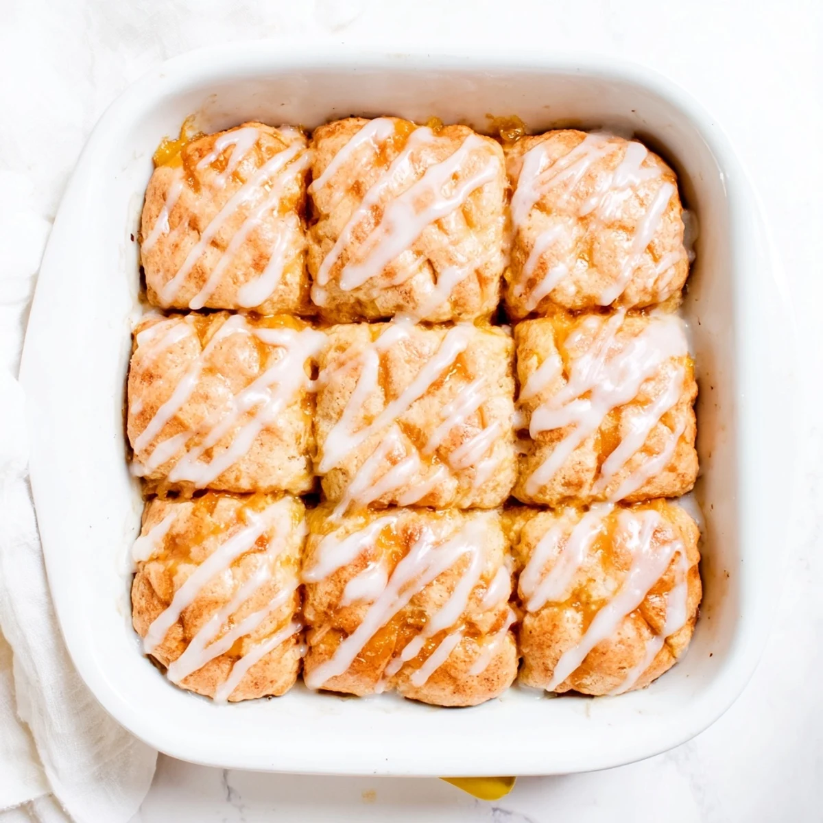 Fluffy buttery biscuits baked in sweet peach butter with vanilla icing on top