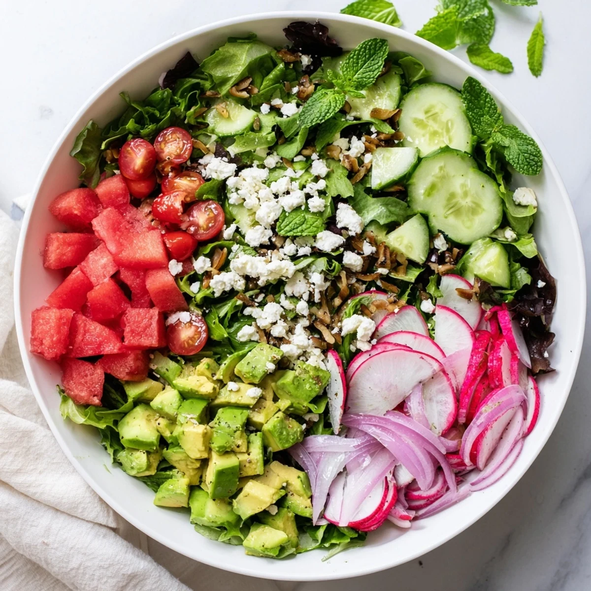 Colorful ultimate summer salad bowl featuring mixed greens, juicy watermelon, cherry tomatoes, and creamy avocado with feta
