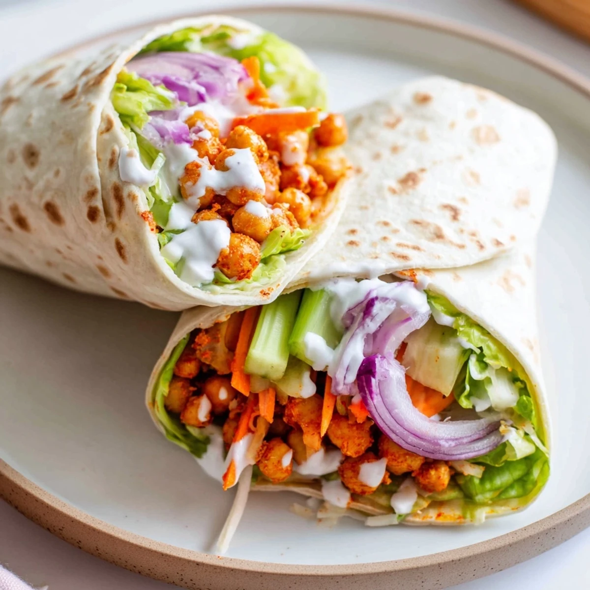 Spicy buffalo chickpea wrap folded with fresh vegetables and drizzled with cool dressing for contrast