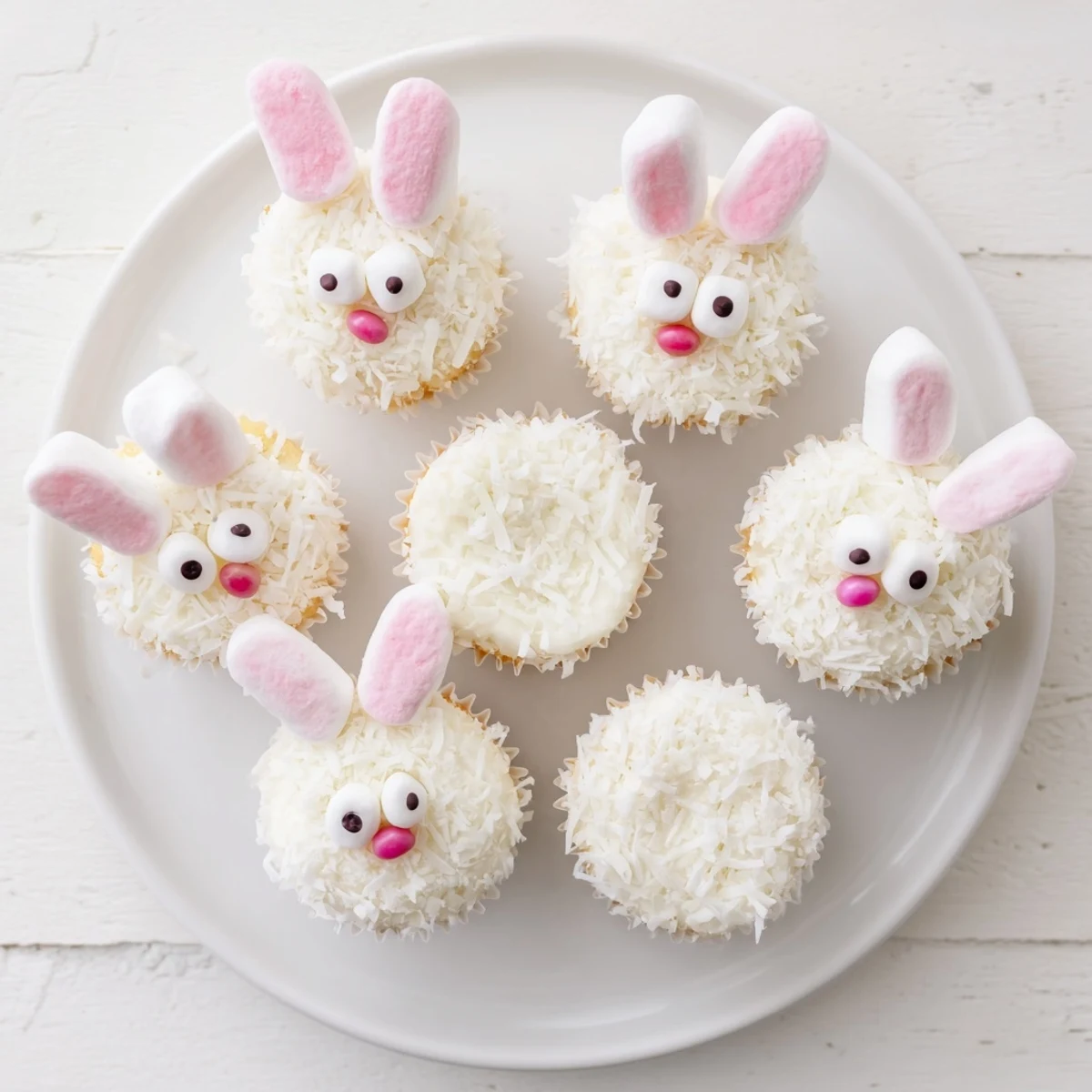 Easter bunny cupcakes decorated with white coconut, pink glitter marshmallow ears, and jelly bean noses