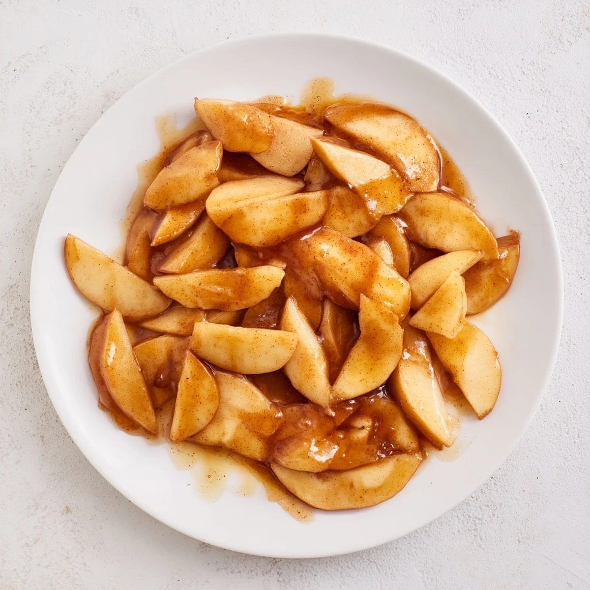Golden brown apple slices coated in cinnamon sugar syrup served in a white bowl