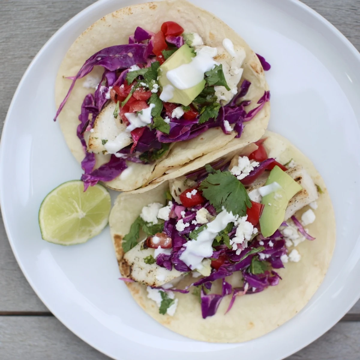 Golden grilled fish tacos topped with fresh cilantro, crunchy cabbage, and creamy lime sauce on warm corn tortillas