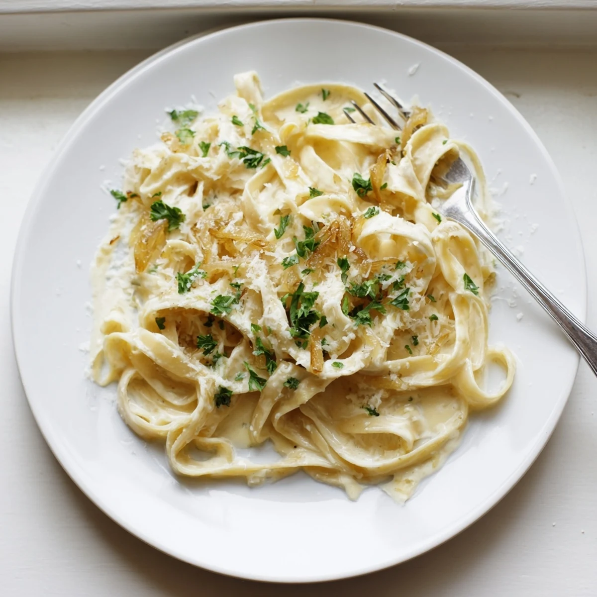 Creamy caramelized onion pasta dish with tender fettuccine swimming in a luxurious white cream sauce