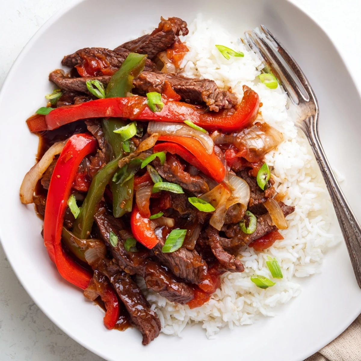 Hearty Slow Cooker Pepper Steak served over fluffy white rice with sliced green onions garnish