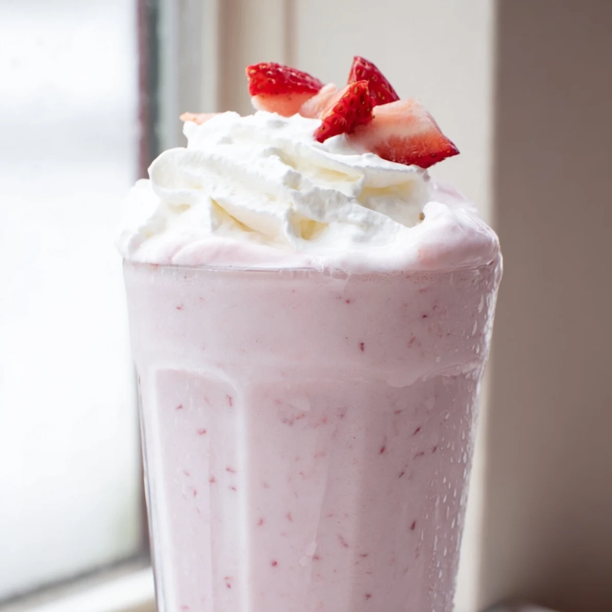 A thick strawberry milkshake topped with whipped cream and fresh berry slices
