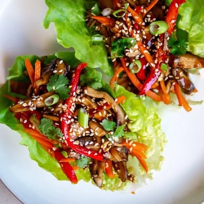 Freshly sautéed shiitake mushroom lettuce wraps garnished with sesame seeds and cilantro on a rustic wooden serving board.