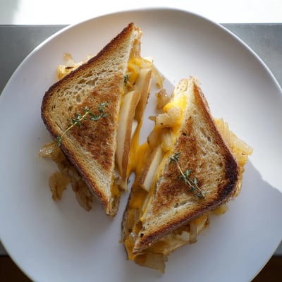 A close-up of the open-faced Pear, Apple & Graved Cheese with Caramelized Onions, featuring thin pear and apple slices on crispy buttered sourdough.