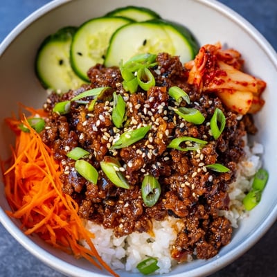 Savory Korean ground beef bowl drizzled with glossy sweet-spicy sauce over jasmine rice with fresh cucumbers